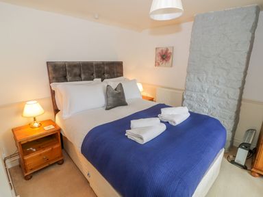 A bedroom with a double bed with white sheets and blue blanket and towels on it two wooden bedside tables with lamps and a stone wall at 4 Lansdown Cottages Bourton-On-The-Water