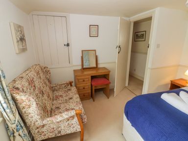 A bedroom with a floral sofa wooden dressing table with mirror and stool a bed with blue cover and white towels on top at 4 Lansdown Cottages in Bourton-On-The-Water