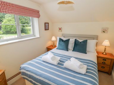 A bedroom with a bed with blue striped blanket and rolled towels next to two wooden nightstands with lamps at 4 Lansdown Cottages in Bourton-On-The-Water