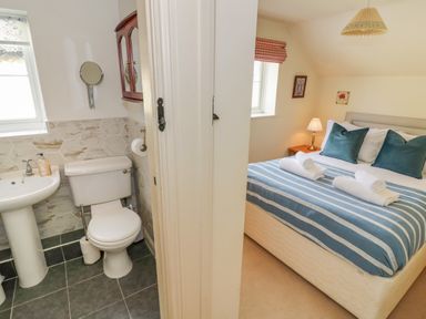 A bathroom with a toilet and sink next to a bedroom with a bed with striped bedding and pillows at 4 Lansdown Cottages Bourton-On-The-Water