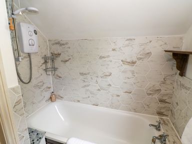 A bathroom with a bathtub showerhead water controls and hexagonal tiled walls at 4 Lansdown Cottages in Bourton-On-The-Water