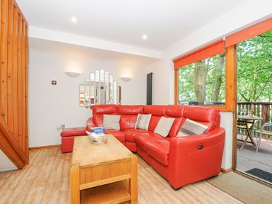 A living room with a red sectional sofa wooden coffee table and a large window at Lodge Nine in Finlake Holiday Park near Chudleigh