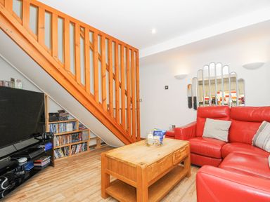 A living room with a red sectional sofa a wooden coffee table a large flat screen tv and wooden staircase with shelves underneath at Lodge Nine in Finlake Holiday Park near Chudleigh