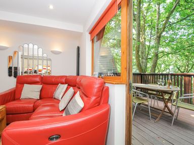 A living room with a red sectional sofa and pillows next to a window looking out onto a balcony with a table and chairs at Lodge Nine in Finlake Holiday Park near Chudleigh