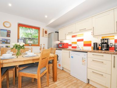 A kitchen with dining table set with dishes and glasses a window fridge dishwasher and red microwave at Lodge Nine in Finlake Holiday Park near Chudleigh
