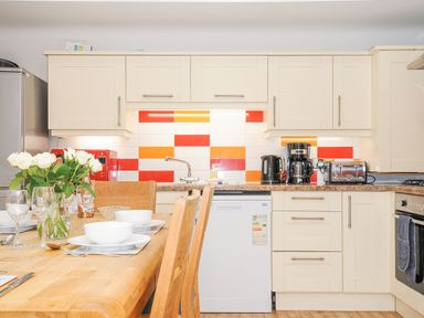 A kitchen with white cabinets colorful tiles and a wooden dining table set with dishes at Lodge Nine Finlake Holiday Park near Chudleigh