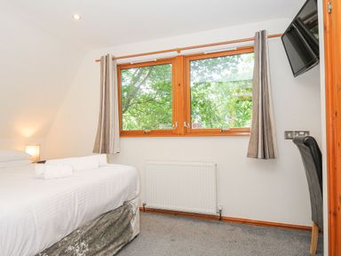 A bedroom with a bed and folded towels near a window with curtains and a wall-mounted television at Lodge Nine in Finlake Holiday Park near Chudleigh
