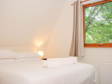 A bedroom with a bed with white linens and rolled towels by a window with curtains at Lodge Nine in Finlake Holiday Park near Chudleigh