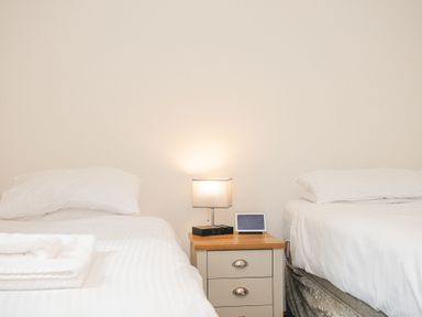 A bedroom with two single beds and a nightstand with a lamp and a digital clock between them