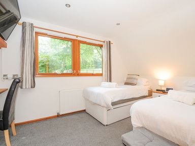A bedroom with two single beds a wooden window a desk with a chair and a wall-mounted television at Lodge Nine Finlake Holiday Park near Chudleigh