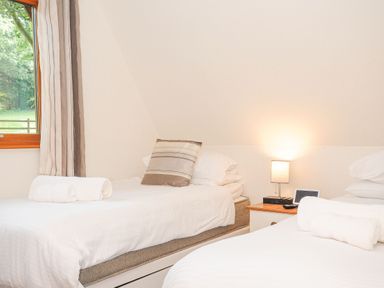A bedroom with two single beds with white linens and a bedside table with a lamp and electronic device at Lodge Nine Finlake Holiday Park near Chudleigh