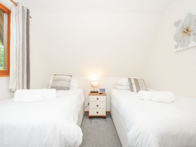 A bedroom with two single beds a nightstand with a lamp and window with striped curtains at Lodge Nine Finlake Holiday Park near Chudleigh