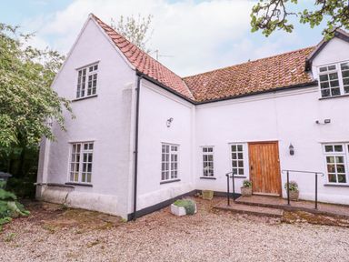 Exterior of a white house with multiple windows a wooden door and a gravel ground with plants at White House Cottage in Little Snoring near Fakenham