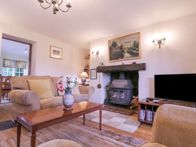 A living room with a sofa and a coffee table with flowers a fireplace and a television at White House Cottage in Little Snoring near Fakenham