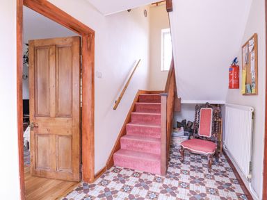A hallway with a patterned tiled floor a wooden door an upholstered chair red carpeted stairs and a fire extinguisher on the wall at White House Cottage in Little Snoring near Fakenham