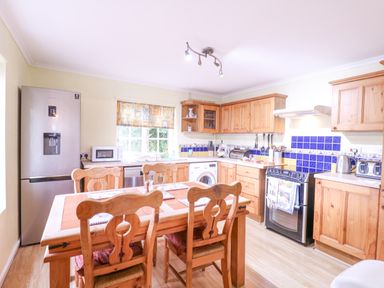 A kitchen with wooden cabinets a dining table with chairs a refrigerator and a stove at White House Cottage in Little Snoring near Fakenham