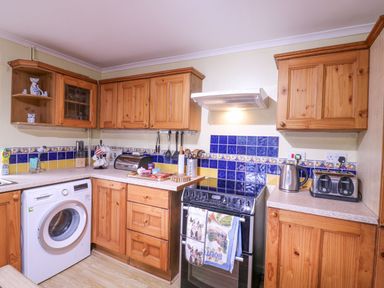 A kitchen with wooden cabinets a washing machine stove kettle toaster and kitchen utensils at White House Cottage in Little Snoring near Fakenham