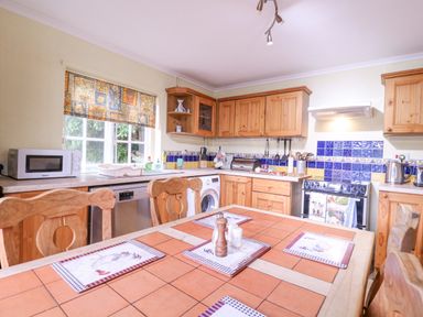 A kitchen with wooden cabinets a tiled table and window with a patterned blind at White House Cottage in Little Snoring near Fakenham