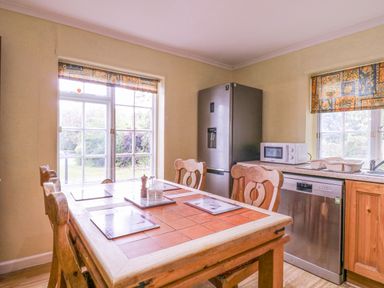 A kitchen with a wooden dining table and chairs a refrigerator dishwasher and microwave at White House Cottage in Little Snoring near Fakenham