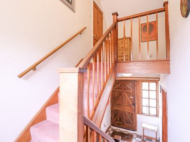 An entryway with wooden staircase carpeted stairs a wooden front door and a small table by a window at White House Cottage in Little Snoring near Fakenham