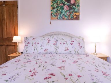 A bedroom with a floral bedspread and pillows a wooden door and two bedside lamps at White House Cottage in Little Snoring near Fakenham
