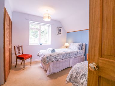 A bedroom with two beds patterned bedding a wooden chair with a red seat and a window at White House Cottage in Little Snoring near Fakenham