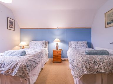 A bedroom with two single beds with patterned bedding a wooden nightstand and lamps at White House Cottage in Little Snoring near Fakenham