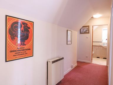 A hallway with red carpet a wall heater and framed pictures on the walls leading to a bathroom at White House Cottage in Little Snoring near Fakenham