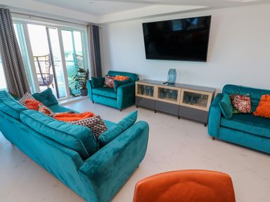 A living room with teal sofas and a large wall mounted television at 17 Cliff Edge in Newquay