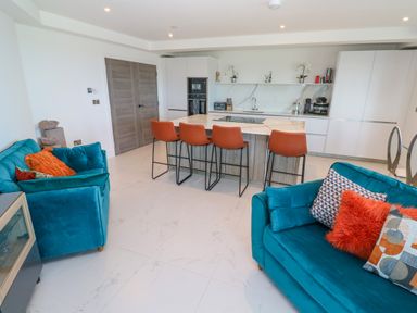 An open-plan kitchen and living area with blue sofas and orange chairs around a kitchen island at 17 Cliff Edge in Newquay