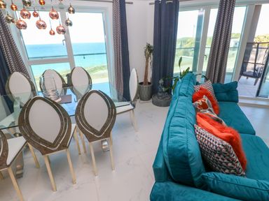 A dining area with glass table and unique chairs next to a seating area with turquoise sofa and colorful cushions at 17 Cliff Edge in Newquay
