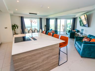 An open-plan kitchen and living area with a marble island and orange bar stools at 17 Cliff Edge in Newquay
