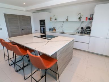 A kitchen with a marble island and four orange bar stools at 17 Cliff Edge in Newquay