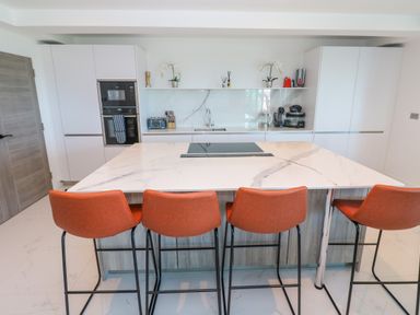 A modern kitchen with a large marble island and four orange bar stools at 17 Cliff Edge in Newquay