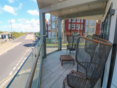 A balcony with chairs and a small table overlooking a street and buildings at 17 Cliff Edge in Newquay