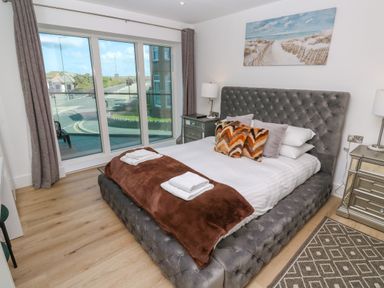 A bedroom with a large tufted bed beside two nightstands with lamps and a large window at 17 Cliff Edge in Newquay