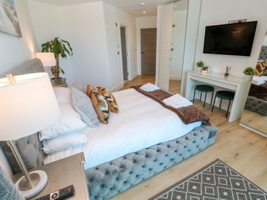 A bedroom with a bed pillows and a blanket two towels on the bed a desk with two stools a TV on the wall and a plant at 17 Cliff Edge in Newquay