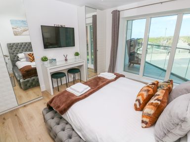 A bedroom with a bed pillows TV wall desk with stools and sliding glass doors at 17 Cliff Edge in Newquay