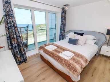 A bedroom with a bed near sliding glass doors with ocean view at 17 Cliff Edge in Newquay