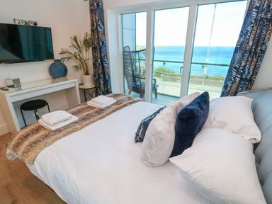 A bedroom with a double bed facing a wall-mounted TV and a balcony overlooking the ocean at 17 Cliff Edge in Newquay