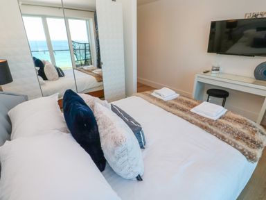 A bedroom with a bed pillows and folded towels by a window and a TV on a wall at 17 Cliff Edge in Newquay