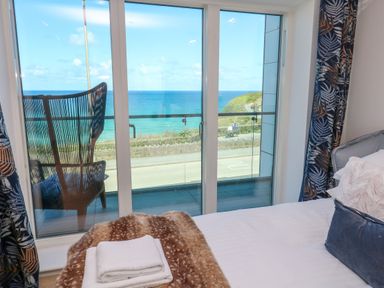 A bedroom with a bed facing sliding glass doors showing a balcony and an ocean view at 17 Cliff Edge in Newquay