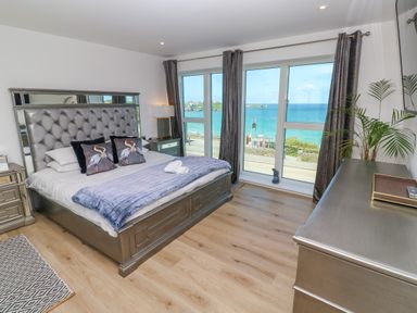 A bedroom with a bed and pillows near large windows overlooking the sea at 17 Cliff Edge in Newquay