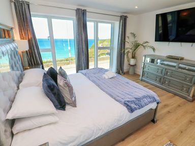 A bedroom with a bed and pillows facing large windows with an ocean view at 17 Cliff Edge in Newquay