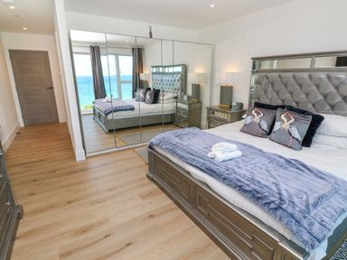 A bedroom with a large bed with decorative pillows and blankets a mirrored wardrobe and a window with ocean view at 17 Cliff Edge in Newquay