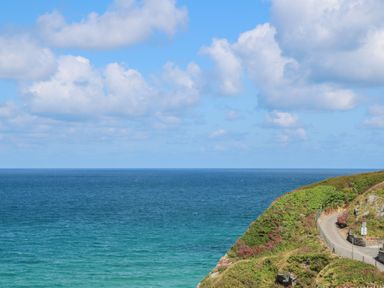 A coastal view with a winding road and green bushes overlooking the ocean at 17 Cliff Edge in Newquay