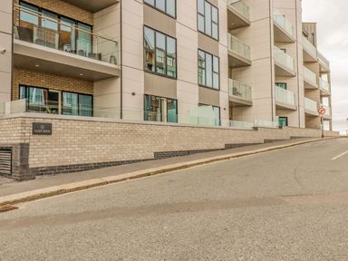 The exterior of a modern apartment building with glass balconies and a brick retaining wall at 17 Cliff Edge in Newquay