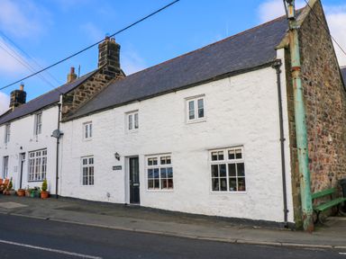 A street view of a white stone cottage with several windows and chimneys at Rose Hip Cottage in Bellingham
