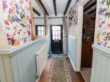 A hallway with floral wallpaper and light blue wainscoting a mirror radiator a rug and a black door at Rose Hip Cottage in Bellingham