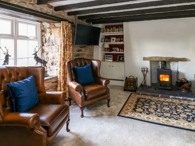 A sitting room with two leather armchairs a fireplace and a wall-mounted TV at Rose Hip Cottage in Bellingham
